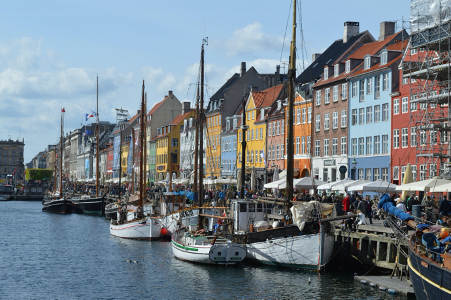 Colourful houses sat on the waterfront of a city in Denmark. There are boats on the water in front of the houses.